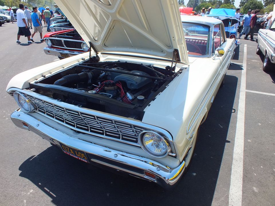 Cream classic Ford with hood up and yellow plate at a car show