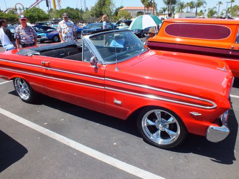 Red classic convertible with chrome wheels at an outdoor car show