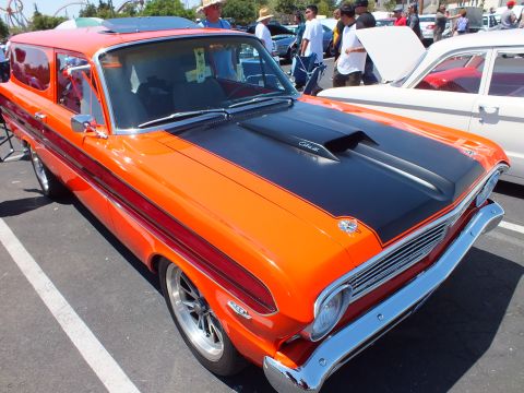 Orange two-door wagon with black hood and chrome wheels at a car show
