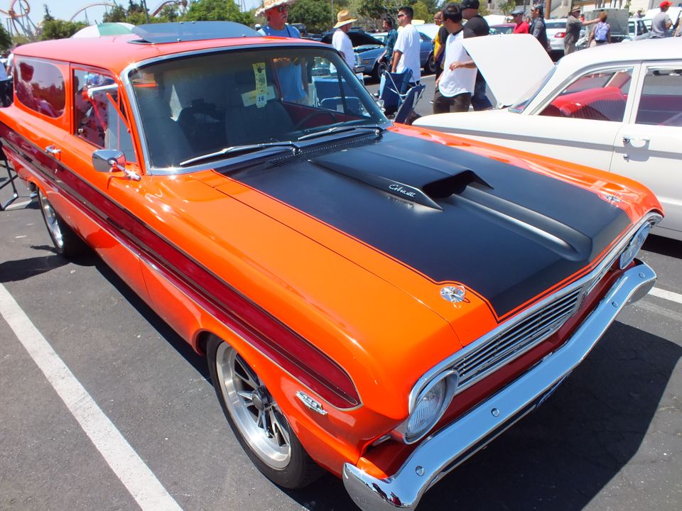 Orange two-door wagon with black hood and chrome wheels at a car show