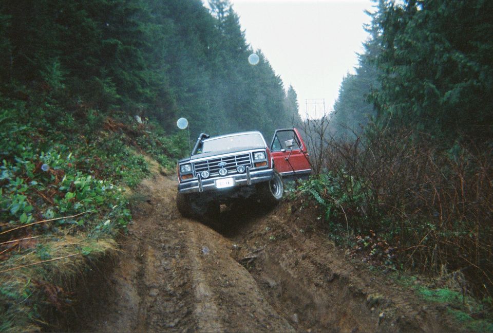 Lifted red and white 1980s Ford Bronco with snorkel on a rutted muddy forest road