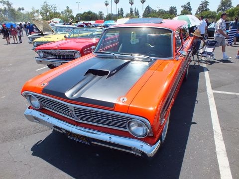 Orange Ford with black scooped hood and yellow plate at a car show