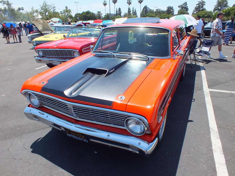 Orange Ford with black scooped hood and yellow plate at a car show