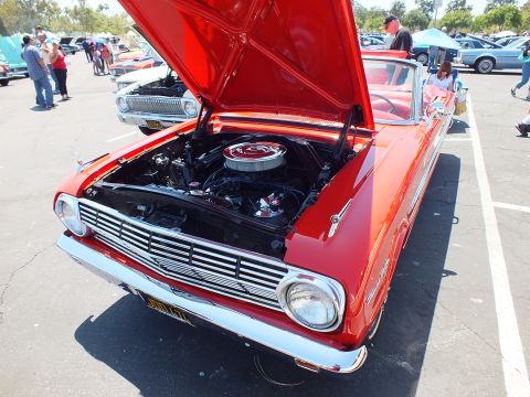 Red early-1960s compact car front view with hood open and air cleaner visible