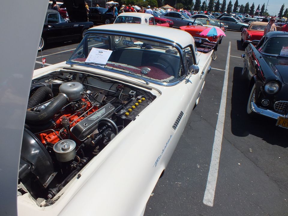 White two-seat hardtop with hood open showing orange-painted V8 at car show