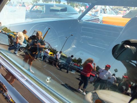 Reflections of a car show crowd and vehicles in a car's windshield glass