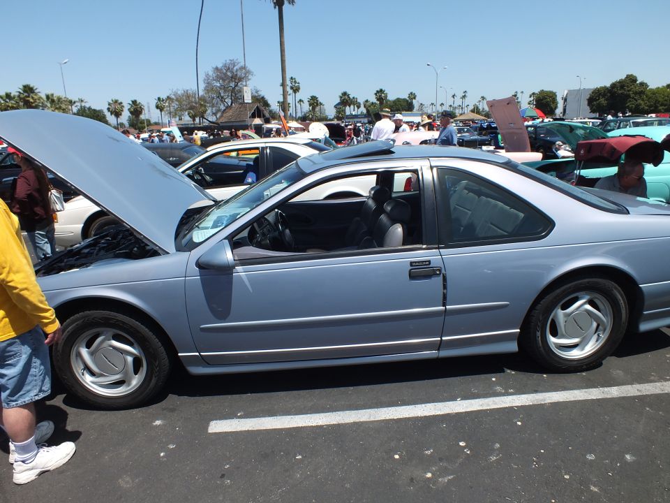 Silver-blue 1990s coupe side profile with hood open at car show