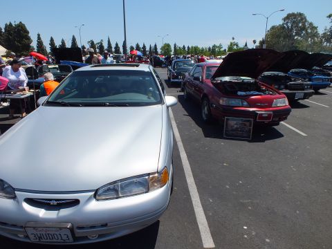 Silver 1990s coupe beside a maroon coupe with hoods up at a car show