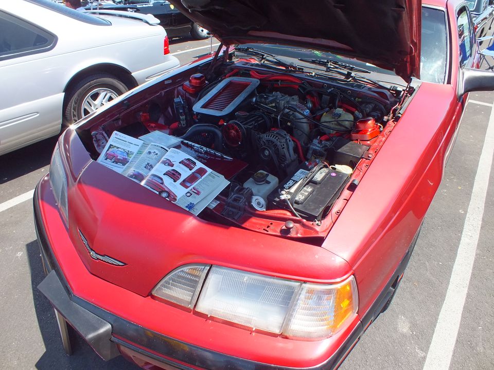 Red coupe with open hood and informational placard on the engine bay