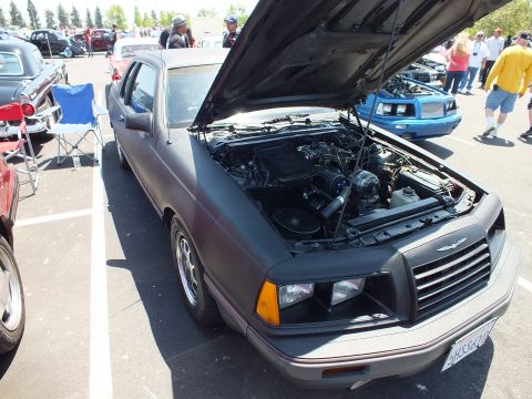 Matte black two-door coupe with open hood at an outdoor car show