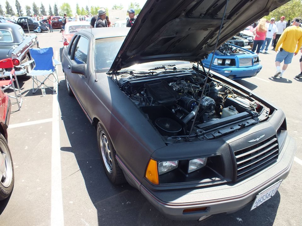Matte black two-door coupe with open hood at an outdoor car show