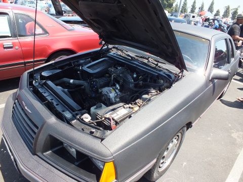 Textured dark gray coupe with open hood showing engine at car show