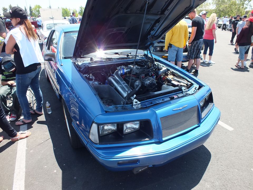 Bright blue coupe with open hood and turbo engine at a car show
