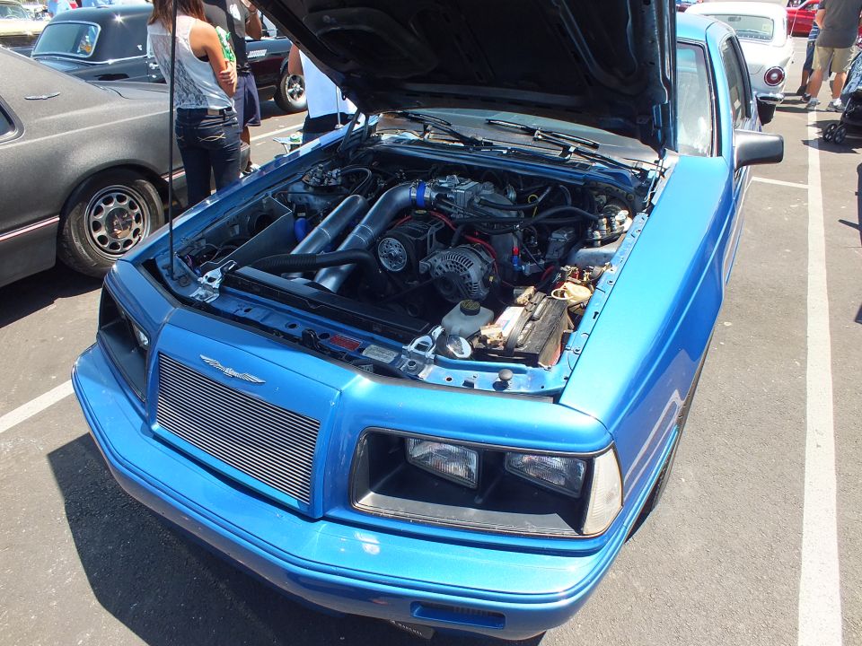 Front of blue coupe with open hood, custom grille and turbo engine