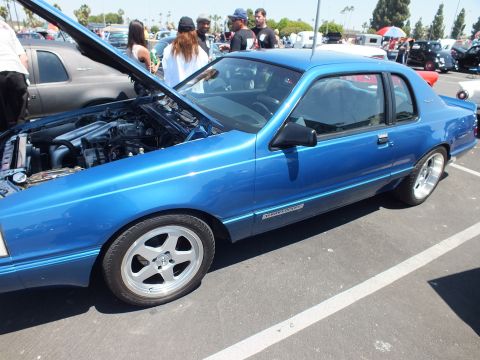 Side view of bright blue lowered coupe with hood up at a car show