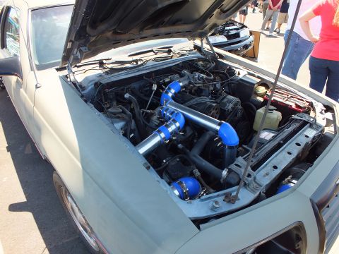 Engine bay with blue intercooler piping under a raised hood at a show
