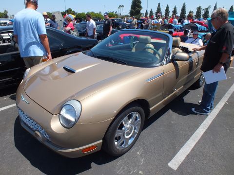 Gold Ford Thunderbird convertible with people inspecting it at a show
