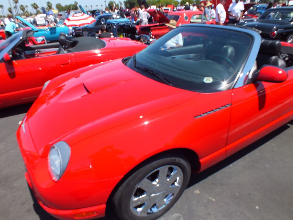 Red two-seat roadster with chrome wheels parked at a car show