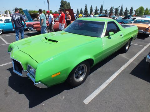 Green car-based pickup with hood scoop parked at outdoor car show