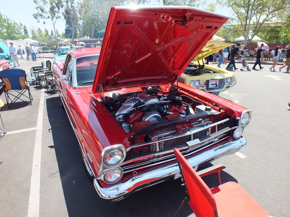 Red classic car with open hood and chrome valve covers at car show