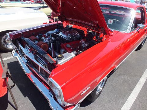 Red classic two-door car with open hood showing engine at car show