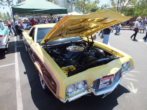 Yellow car-based pickup with open hood and wood-grain trim at car show