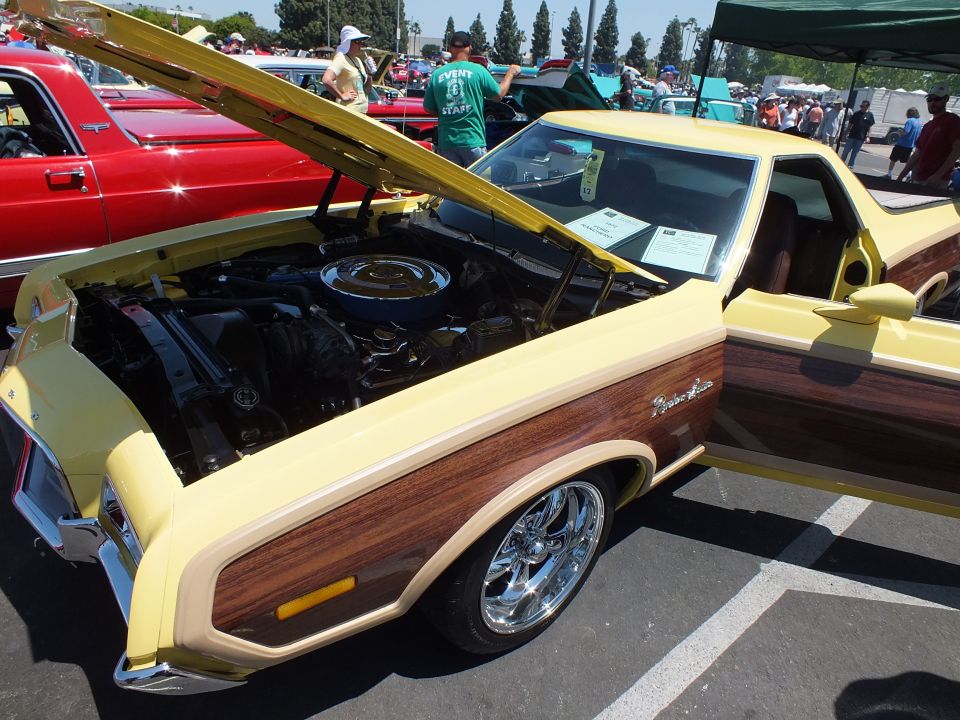 Yellow Ford Ranchero with woodgrain panels and open hood at a car show