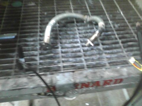 2003 Ford Crown Victoria - A metal pipe rests on a grated surface, with partial red lettering visible on the edge of the grate.