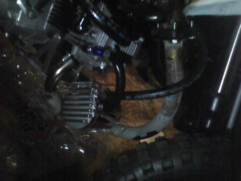 Close-up of motorcycle engine components including hoses and a finned metal part