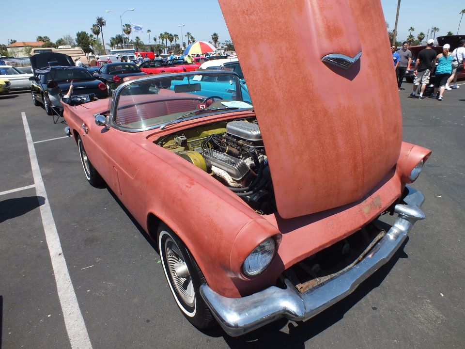 Faded primer-red Ford Thunderbird convertible with hood up at a car show