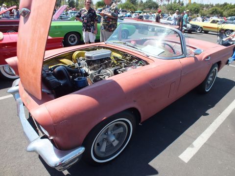 Primer-red Ford Thunderbird with open hood and V8 engine at a car show
