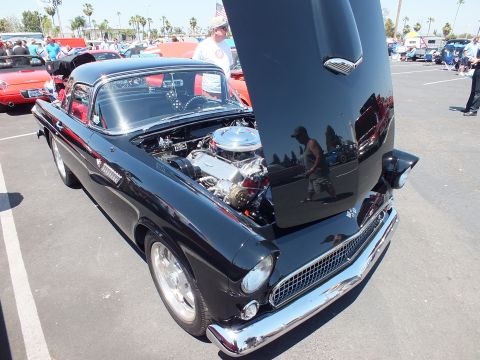 Black first-gen Ford Thunderbird with hood up showing chrome engine at outdoor car show