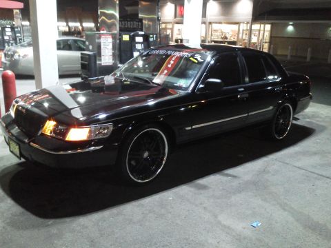 2000 Mercury Grand Marquis - Black 2000 Mercury Grand Marquis with custom wheels at a gas station at night.