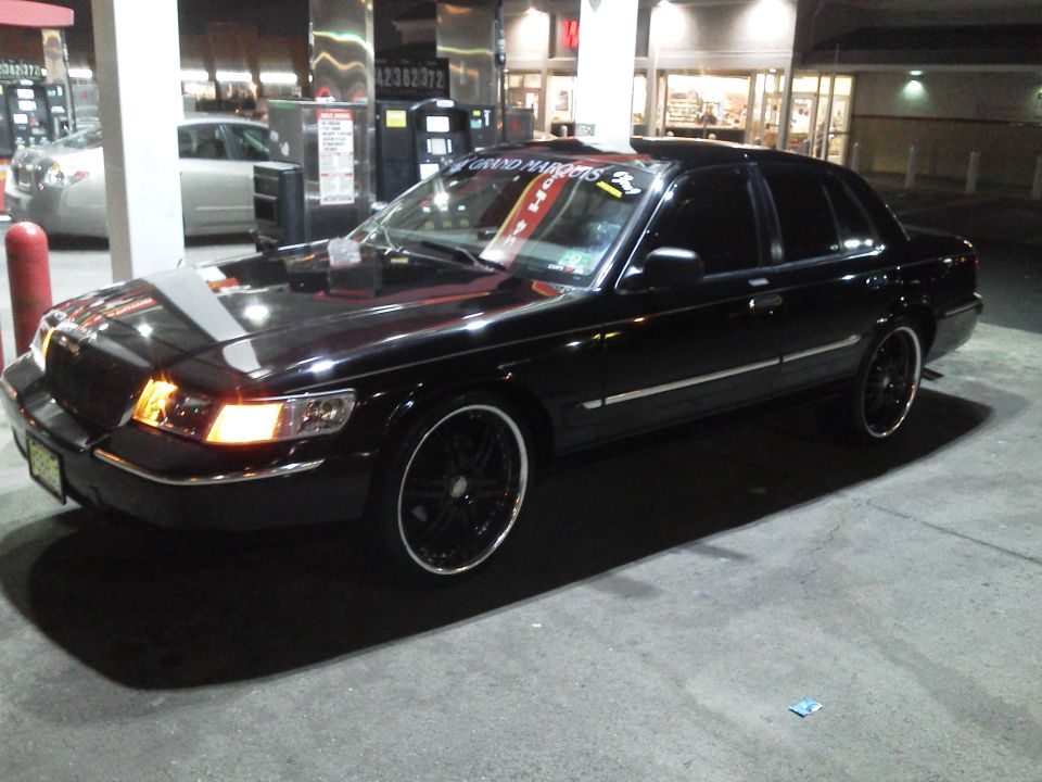 Black 2000 Mercury Grand Marquis parked at gas station, custom rims