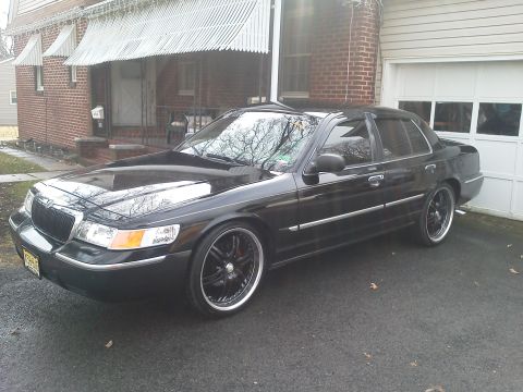 2000 Mercury Grand Marquis - A black 2000 Mercury Grand Marquis is parked in front of a brick house and garage, custom wheels.