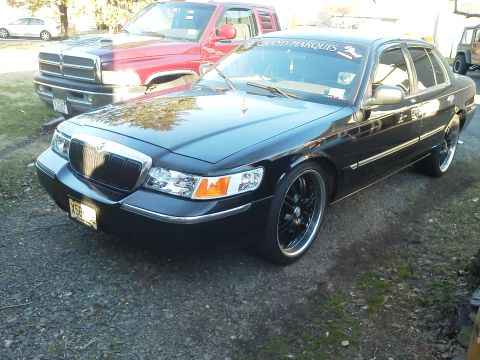 2000 Mercury Grand Marquis - A black 2000 Mercury Grand Marquis sedan is parked outdoors next to a red pickup truck.