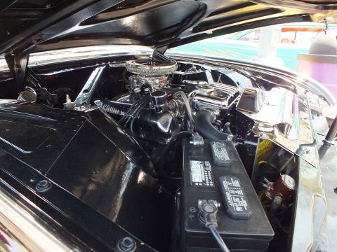 Engine bay of black classic car with chrome carburetor and battery