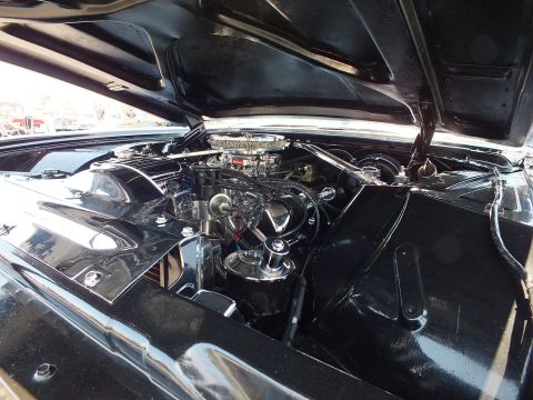 Detailed engine bay of black classic car with chrome carburetor