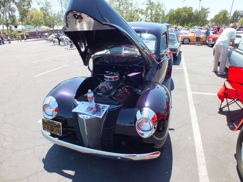 Black late-1930s Ford coupe hot rod with hood open showing chrome V8 engine at a car show