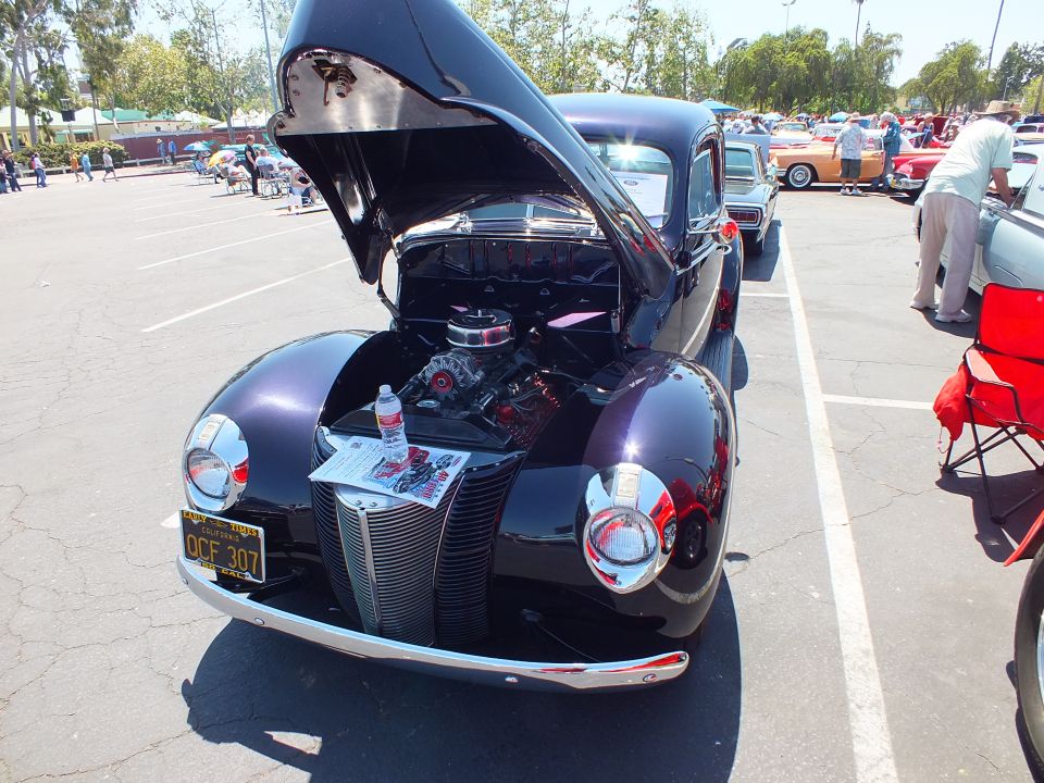 Black late-1930s Ford coupe hot rod with hood open showing chrome V8 engine at a car show