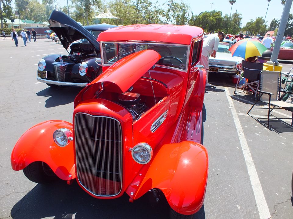 Red 1930s Ford coupe hot rod with open hood showing engine at a car show