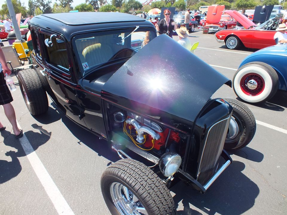 Black highboy roadster-style hot rod with flame engine art and whitewall tire nearby