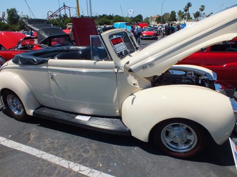 Cream-colored 1940 Ford convertible hot rod with open hood and For Sale sign at car show