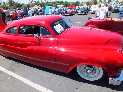 Red chopped custom lead-sled coupe with skirts and whitewall hubcap wheels at car show
