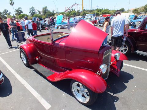 Candy-red Ford roadster hot rod with tan interior and open trunk at outdoor car show