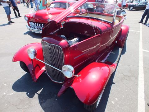 Deep red Ford roadster hot rod with open hood and chrome grille at car show