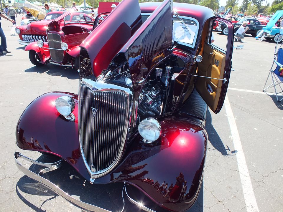 Maroon 1934 Ford coupe hot rod with V-badge grille and open hood and door at car show