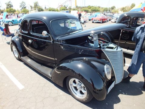 Black 1937-38 Ford coupe hot rod with open hood and chrome grille at car show