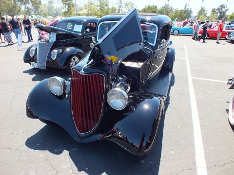 Black 1934 Ford coupe hot rod with maroon grille and open hood at car show