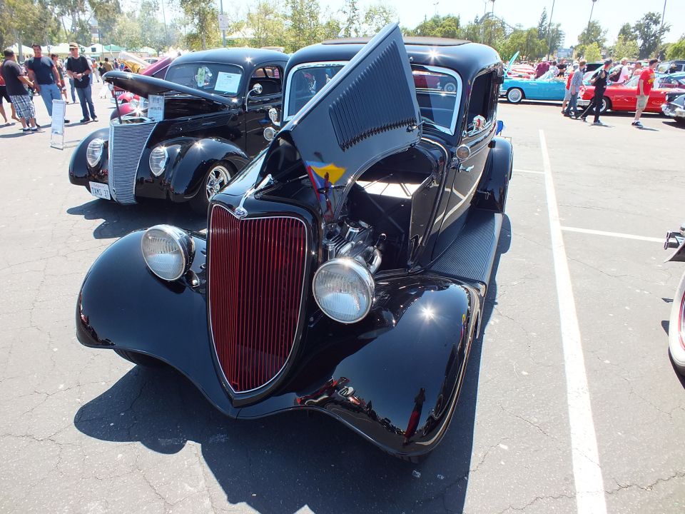 Black 1934 Ford coupe hot rod with maroon grille and open hood at car show